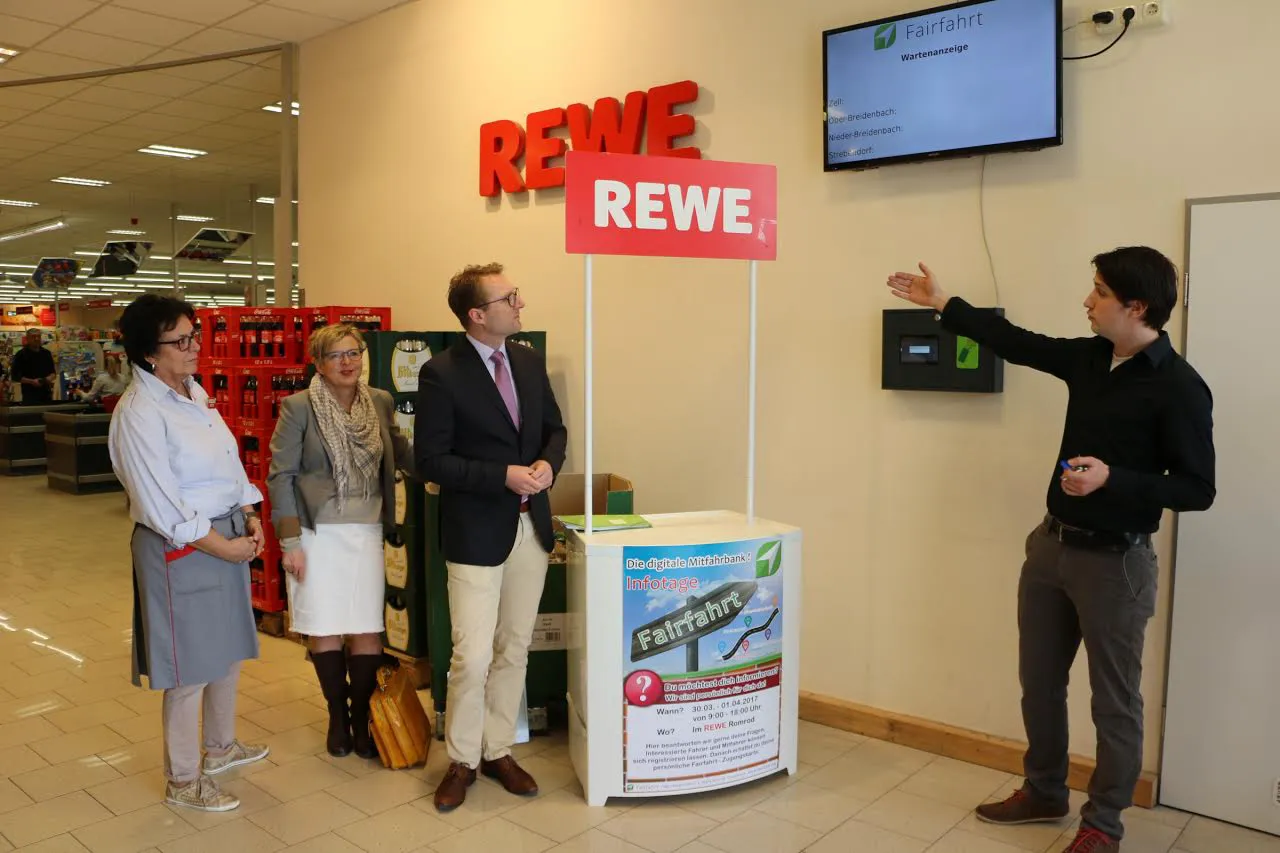 Jonathan Waschkewitz (NetFair Solutions GbR, re.) erklärt „Fairfahrt“ – eine digitale Mitfahrbank für Fahrten zwischen dem REWE-Markt in Romrod und den Stadtteilen. Wirtschaftsdezernent Mischak und Bürgermeisterin Richtberg nahmen den Prototypen in Augenschein, links im Bild die stellvertretende Geschäftsführerin des Marktes Lieselotte Scharmann. Foto: Gaby Richter